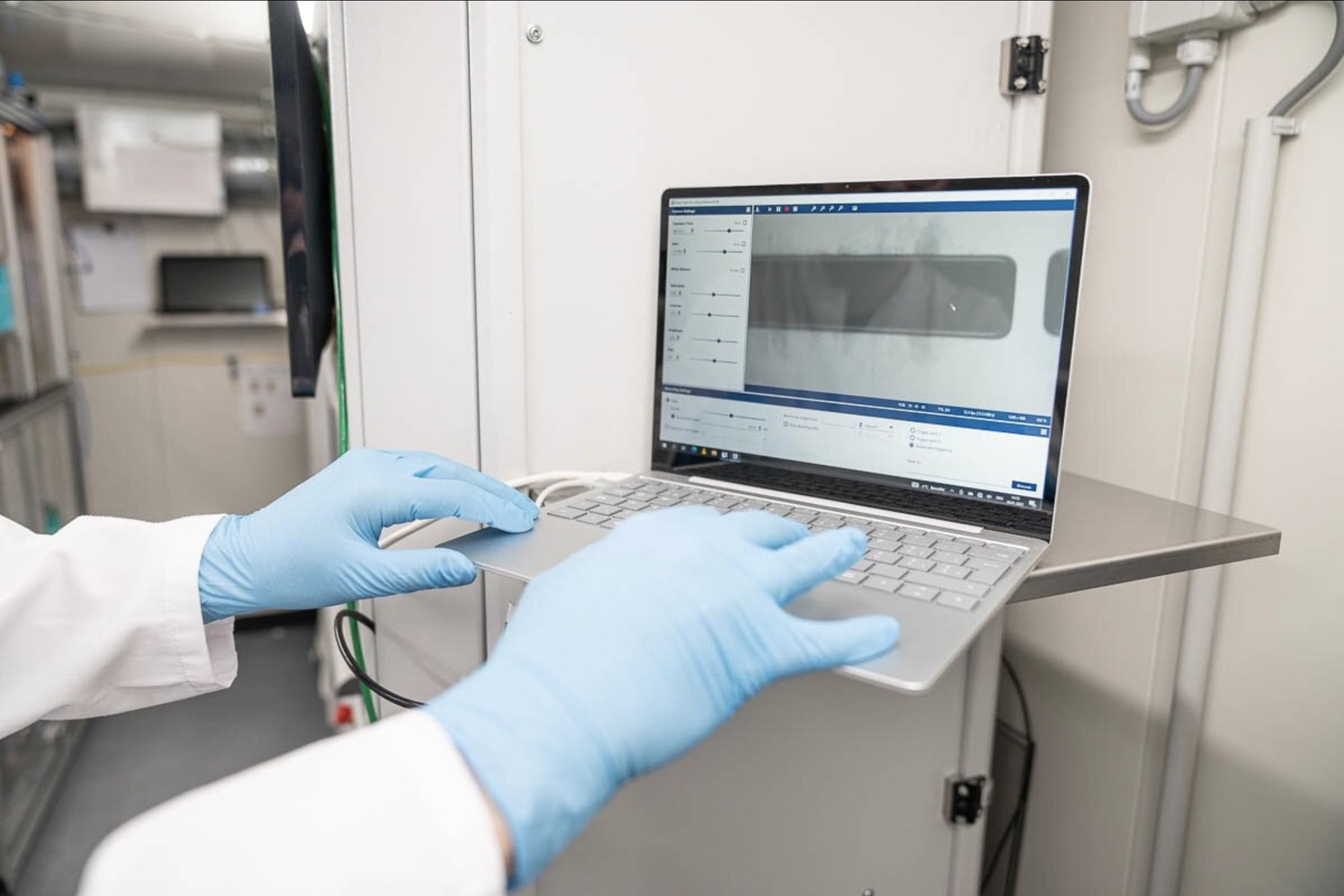 Operator in gloves running the machine software on a laptop inside the laboratory container
