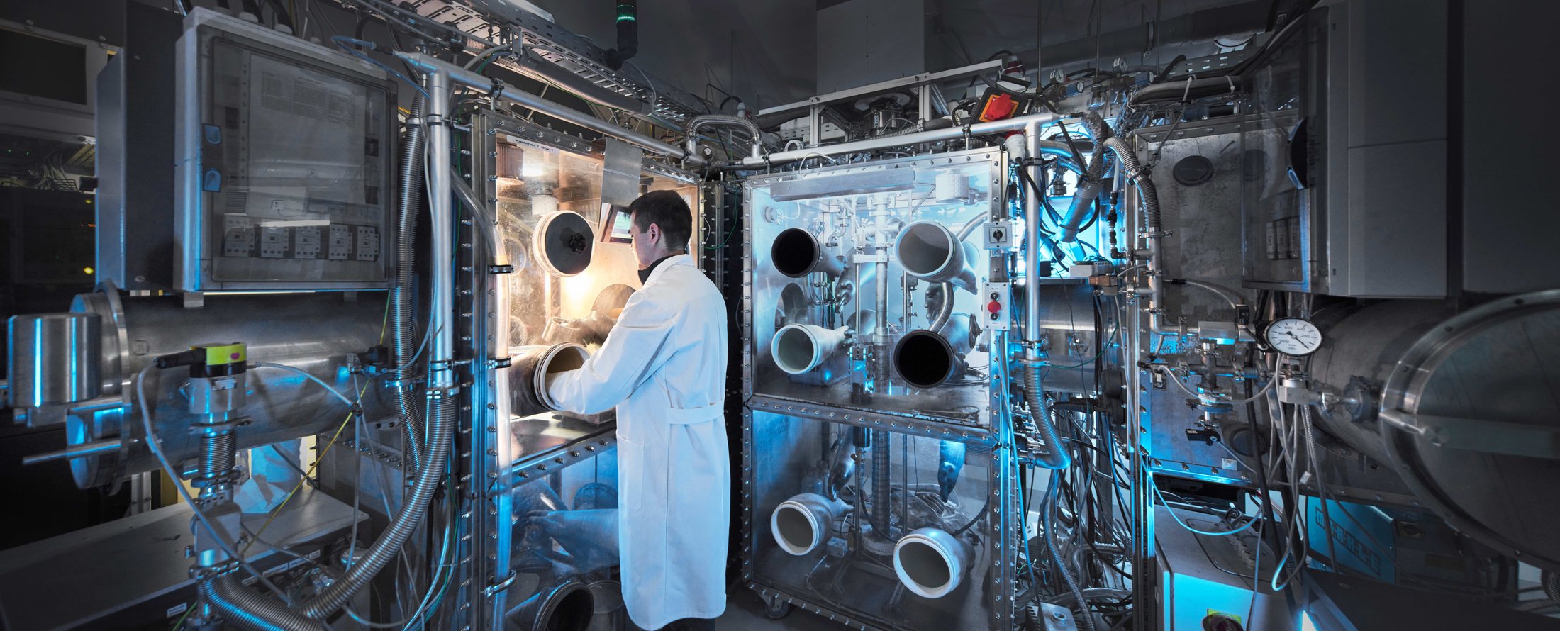 Row of smolsys inert gas glove boxes in a laboratory, operator working at the front box